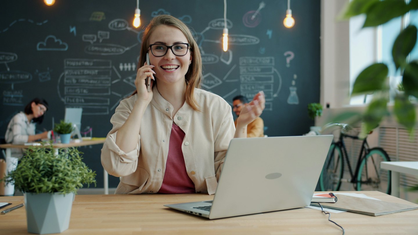 Kobieta w okularach rozmawia przez telefon w nowoczesnym biurze.